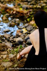 Cropped back view of woman model sitting by a creek in the woods 5oDNx4