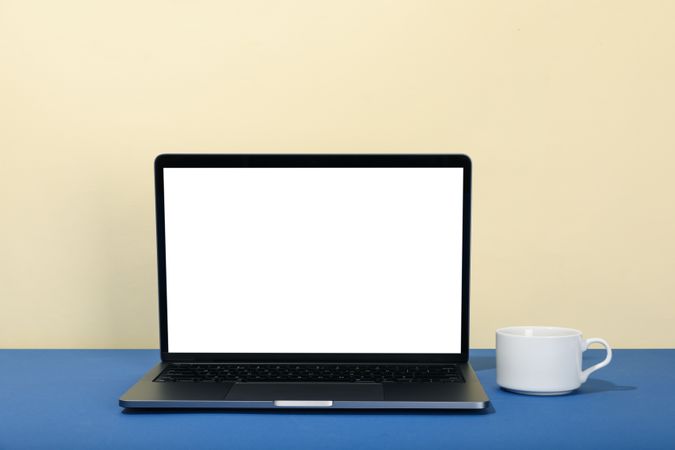 Open laptop with blank mockup screen in cream and blue with cup