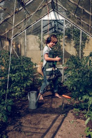 Cheerful boy in headphones working in greenhouse