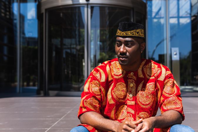 Thoughtful Black man in traditional clothes and headdress near building