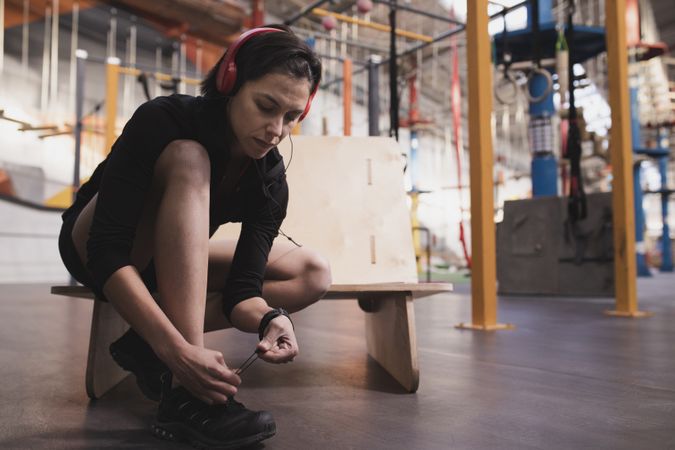 Smiling woman with headphones lacing shoe in gym