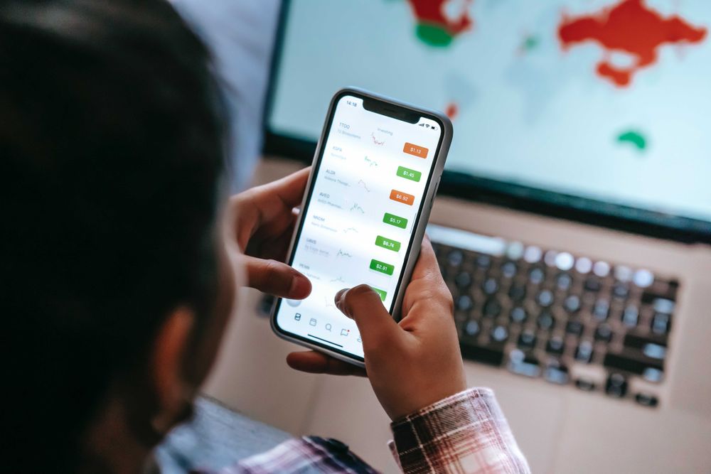 Back view of man checking stock market application using smartphone and computer