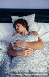 Man sleeping on his back in bed at home holding pillow 56GvzL