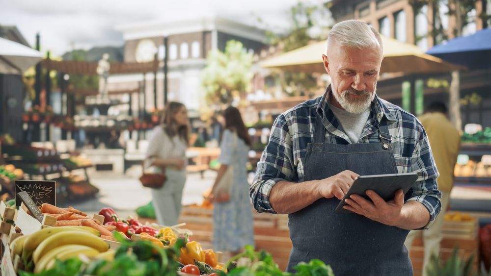 Portrait of an Adult Farmer Using Tablet Computer at Work while Selling Fresh Organic Agricultural Products From a Market Stall.