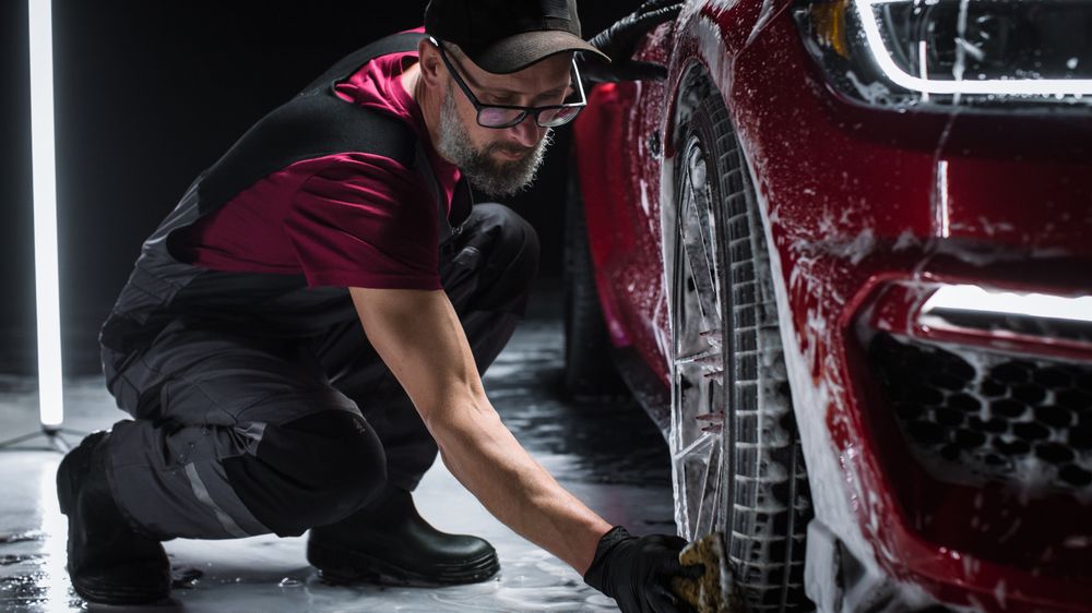 Portrait of an Adult Man Working in a Detailing Studio, Prepping a Factory Fresh American Sportscar for Maintenance Work and Car Care Treatment.