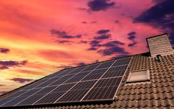 Solar panels producing clean energy on a roof of a residential house during sunset.