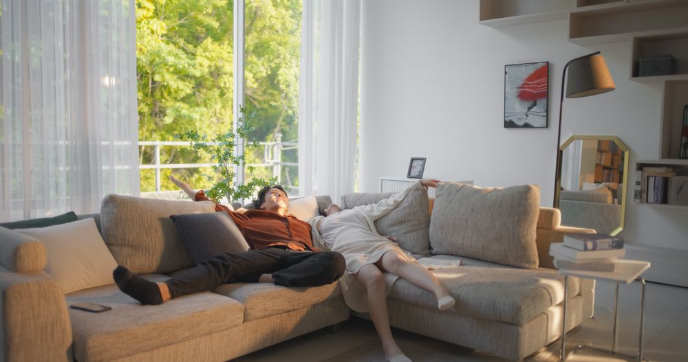 Excited South Korean Couple Fall Down on a Comfortable Sofa in a Stylish Living Room While Smiling.