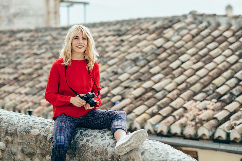 Smiling woman sitting on rocky stoop in Spanish town with SLR camera