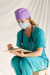 Woman in mask sitting on stool and looking at clipboard