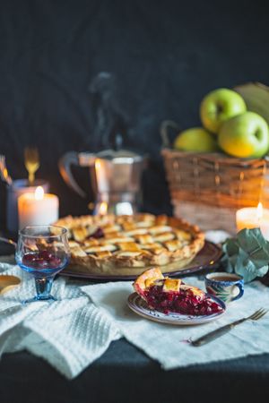 Table setup with cherry pie, candle, espresso pot, and basket of fruit