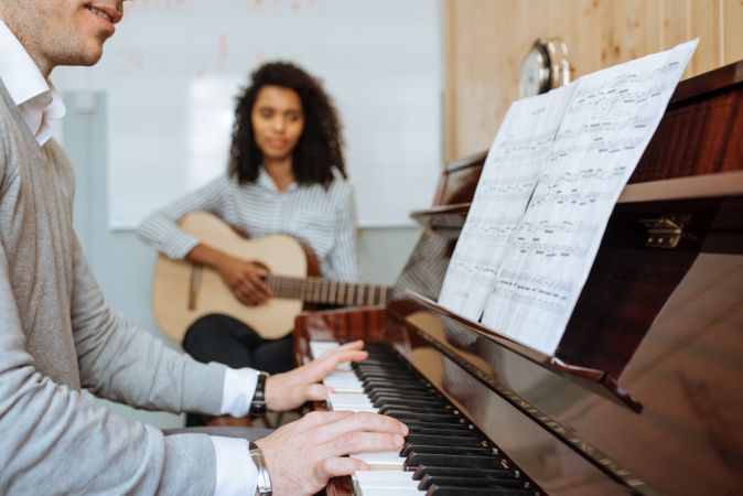 Man playing piano near woman playing guitar in studio