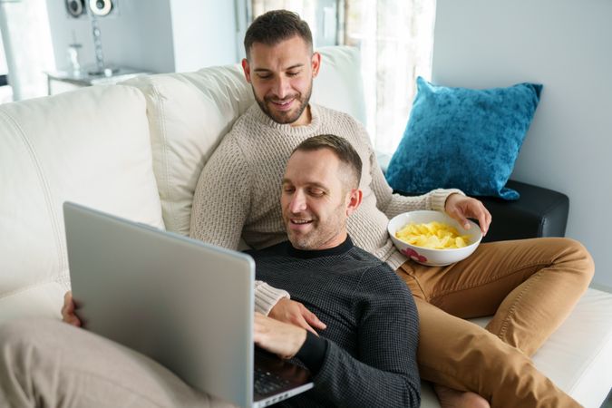 Two men relaxing together on couch reading something on laptop