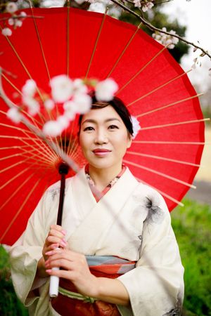Portrait of Japanese woman in light kimono holding a red oil-paper umbrella