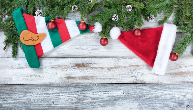 Christmas fir branches along with traditional hat decorations and red ornaments on rustic wooden background