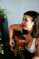 Young woman with straight hair smiling and looking away while holding guitar