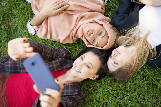 Looking down at three women lying on grass with smartphone