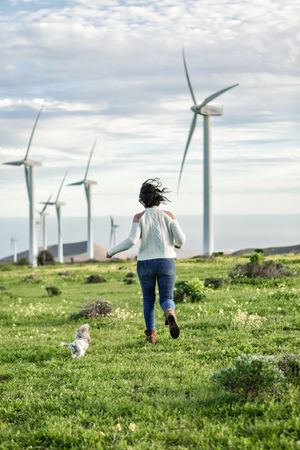 Back view of excited woman running beside wind turbines