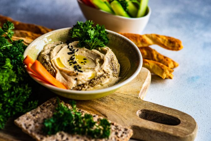 Top view of creamy hummus dip in bowl on board served with veggies and rye crackers