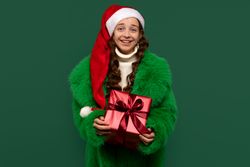 Girl in Santa hat wearing fur coat holding gift box.