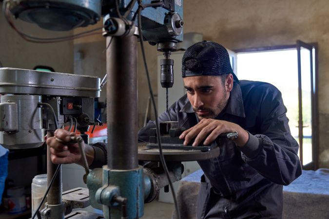 Focused mechanic working with vertical drill in garage