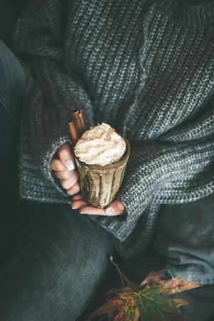 Woman in cozy sweater and jeans holding whipped cream topped drink