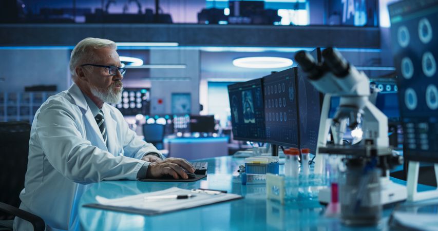 Male Neuroscientist Using Desktop Computer To Analyze MRI Scans Of Brain In Medical Research Center Lab.