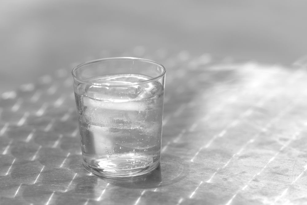 One glass of water with ice on a metallic table outdoors