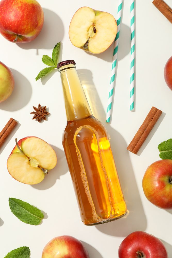 Composition with cider, apples, straws and cinnamon on plain background