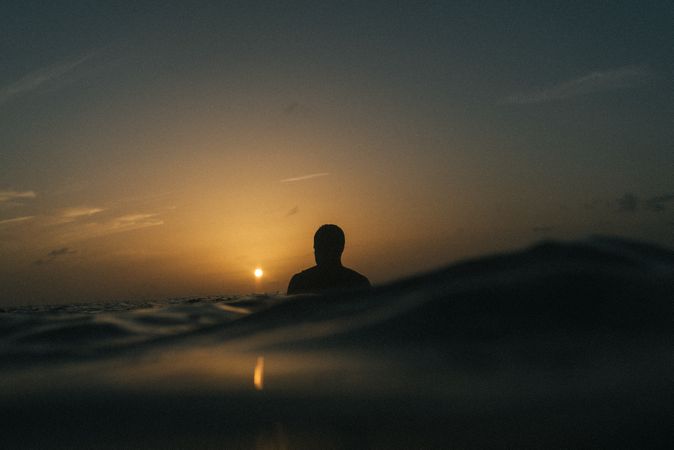 Silhouette of surfer in water at dusk