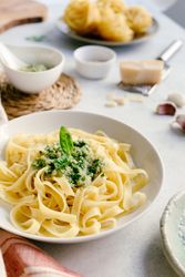 Served plate of pesto pasta next to bowl of sauce on table