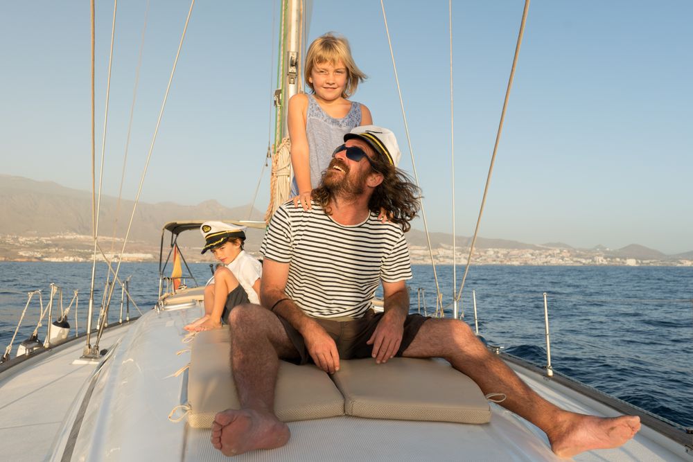 Man with smiling children and sitting on deck of yacht in sea