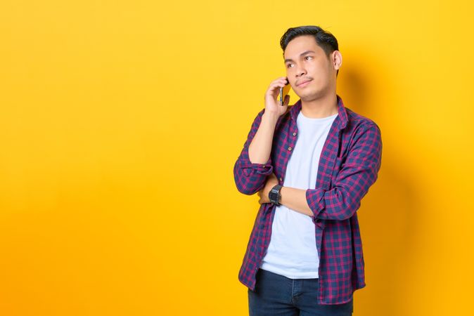Asian male listening on cell phone in yellow studio shoot