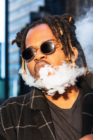 Black man exhaling cloud of smoke on street