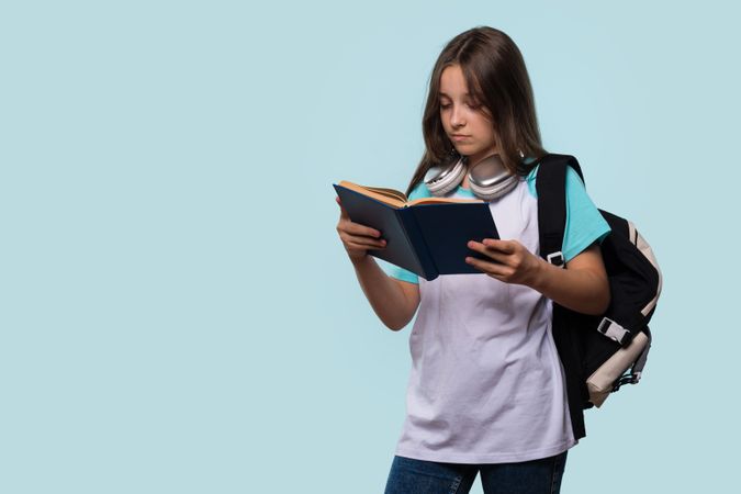 Serious girl reading blue book while carrying backpack