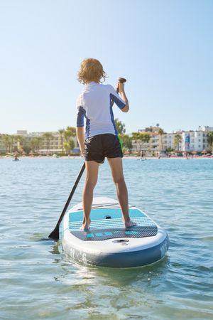 Anonymous child on paddleboard in ocean during summer day