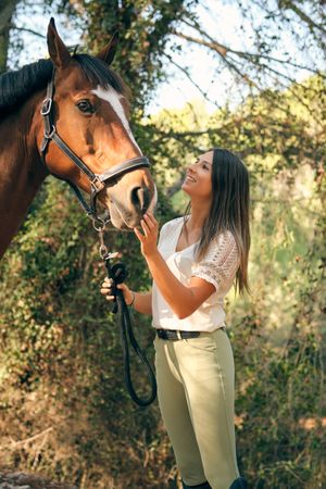 Delighted woman stroking horse in woods