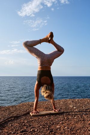 Barefoot sportswoman in Handstand pose on earthy seashore
