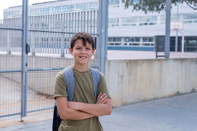 Smiling teenage boy standing outside of school entrance with arms crossed