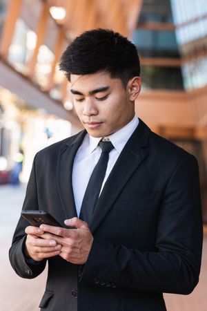 Cheerful Asian male entrepreneur browsing smartphone in city