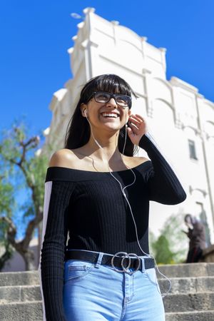 Young stylish woman wearing earphones spending free time outdoors in the sun