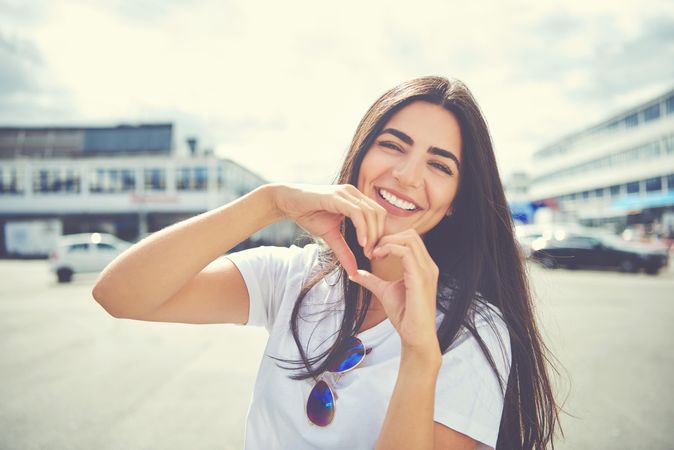 Smiling woman outside near shops making heart shape with hands