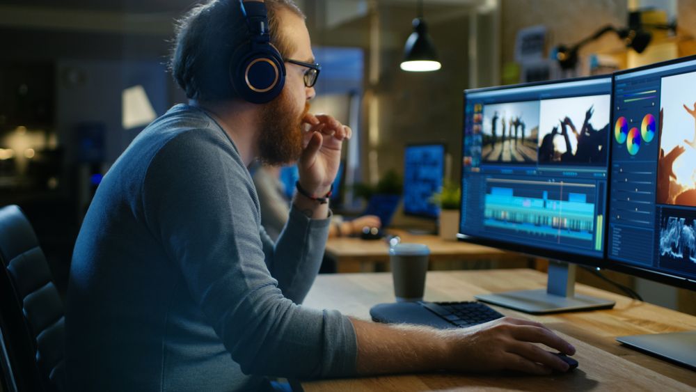 Male Videographer Edits and Cuts Footage and Sound on His Personal Computer, Puts on His Monitors