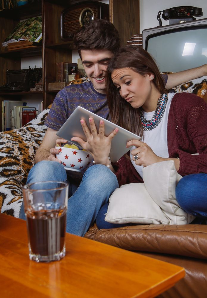 Young couple laughing and looking tablet sitting on sofa