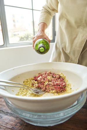 Anonymous person pouring olive oil into bowl with steak tartare