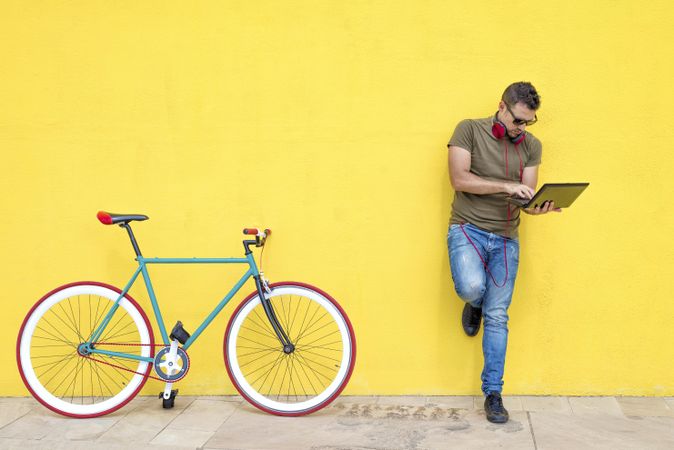 Male with red headphones standing outside with laptop and bicycle
