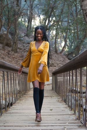 Portrait of a young Black woman with braids wearing a yellow dress walking on a bridge