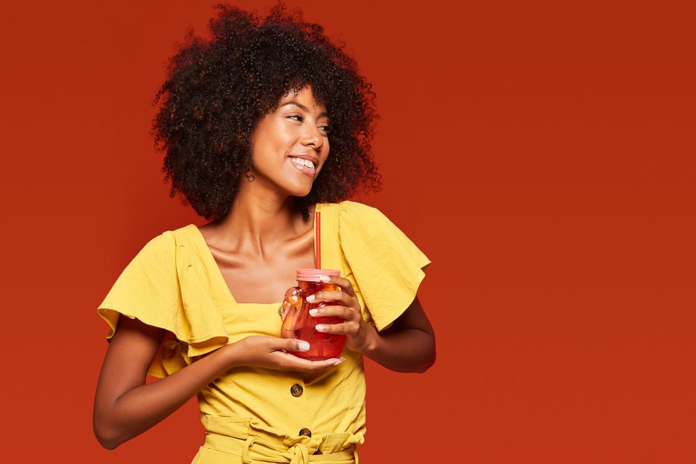 Charming bright Black woman drinking beverage