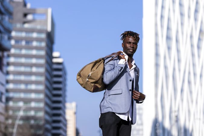 Man wearing elegant jacket, jeans carrying a bag on his back on a sunny day