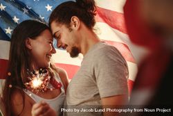 Loving couple holding sparklers wrapped under American flag 0ynnR5