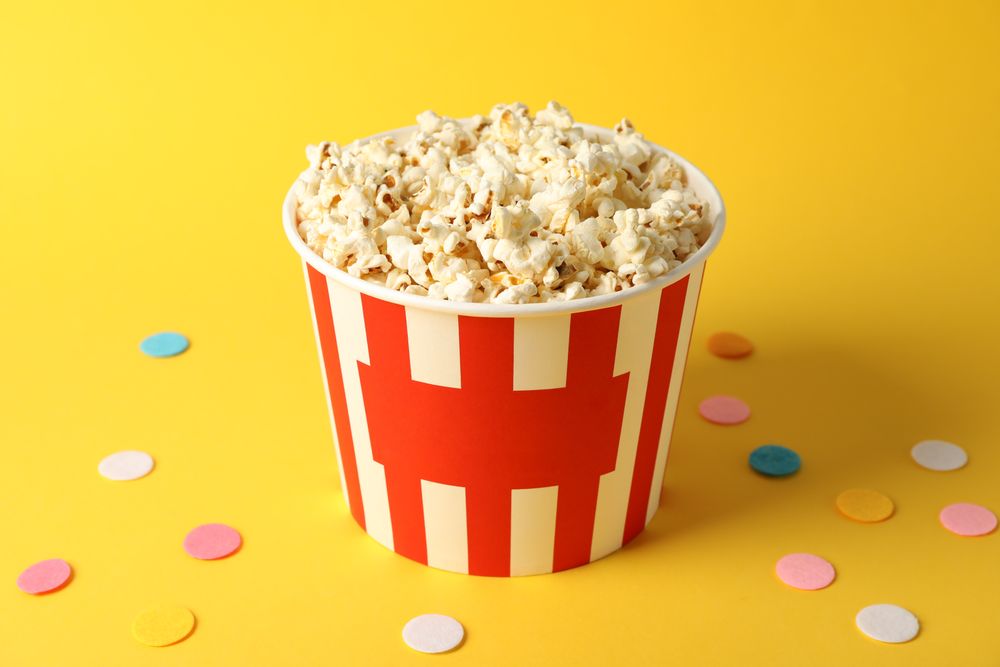 Confetti and bucket with popcorn on yellow background, copy space